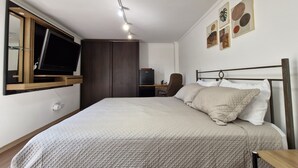 Una habitación de hotel con cama, escritorio, silla, televisor y obras de arte en la pared.