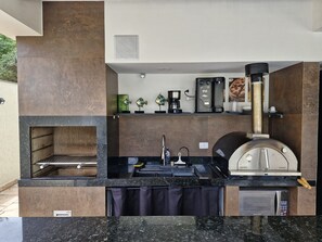 Une cuisine extérieure moderne, dotée d’un barbecue encastré, d’une machine à café et d’un four à pizza.