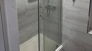 A glass-enclosed shower stall with a white tiled wall, a handheld showerhead, and a control panel. - #127 Modern City Suite | Digbeth Creative Quarter (West Midlands)