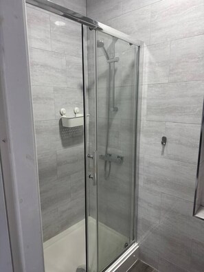 A glass-enclosed shower stall with a white tiled wall, a handheld showerhead, and a control panel. - #127 Modern City Suite | Digbeth Creative Quarter (West Midlands)