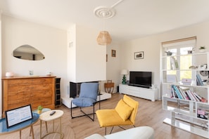 Ein Wohnzimmer mit Sofa, Sessel, Fernseher, Bücherregal und Kamin.