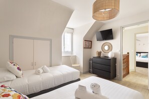 Ein Hotelzimmer mit zwei Betten, einem Fernseher, einem Schreibtisch und Blick auf das Nachbarzimmer.