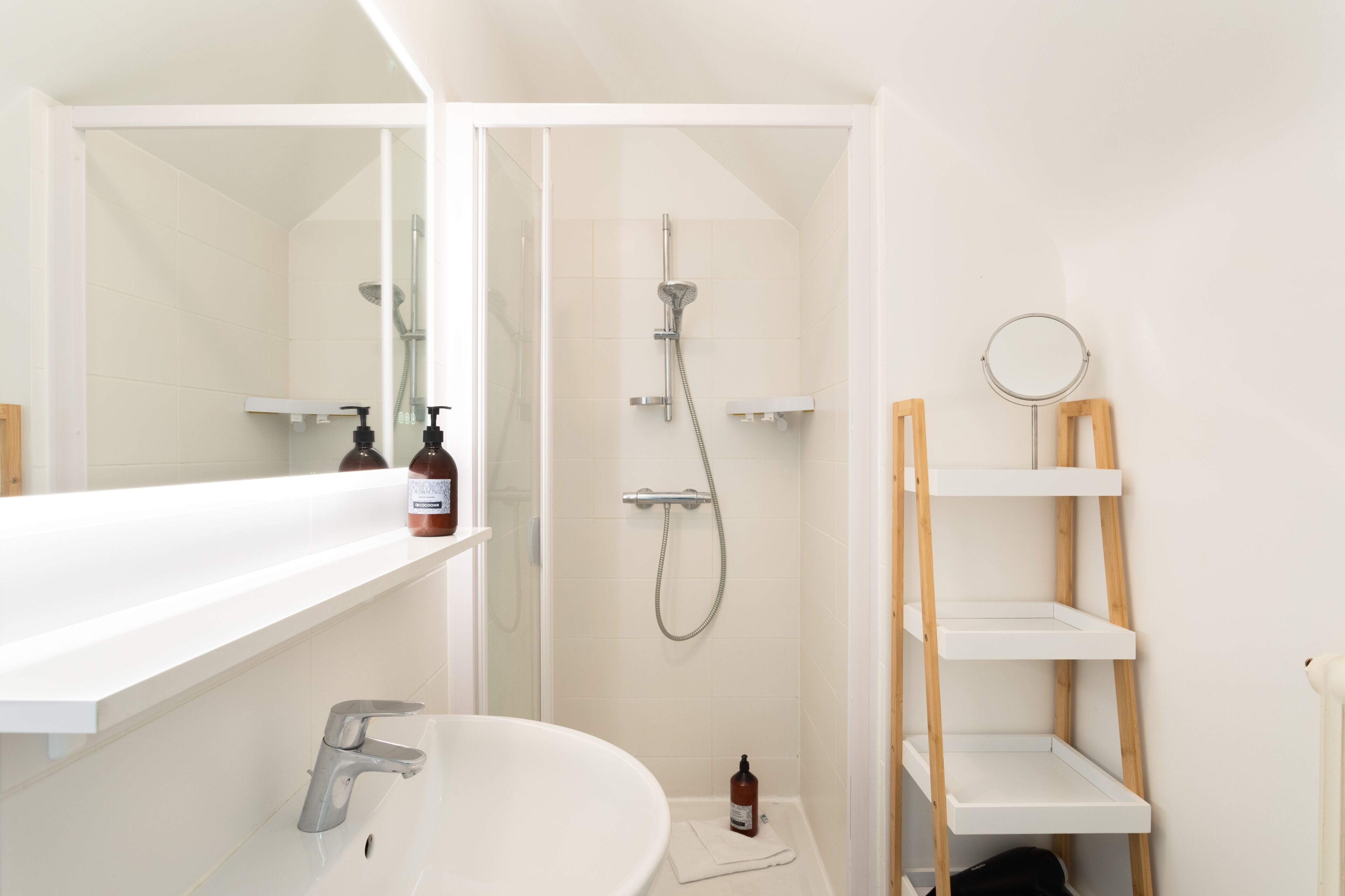 A modern bathroom with a white sink, a shower, and a mirror.