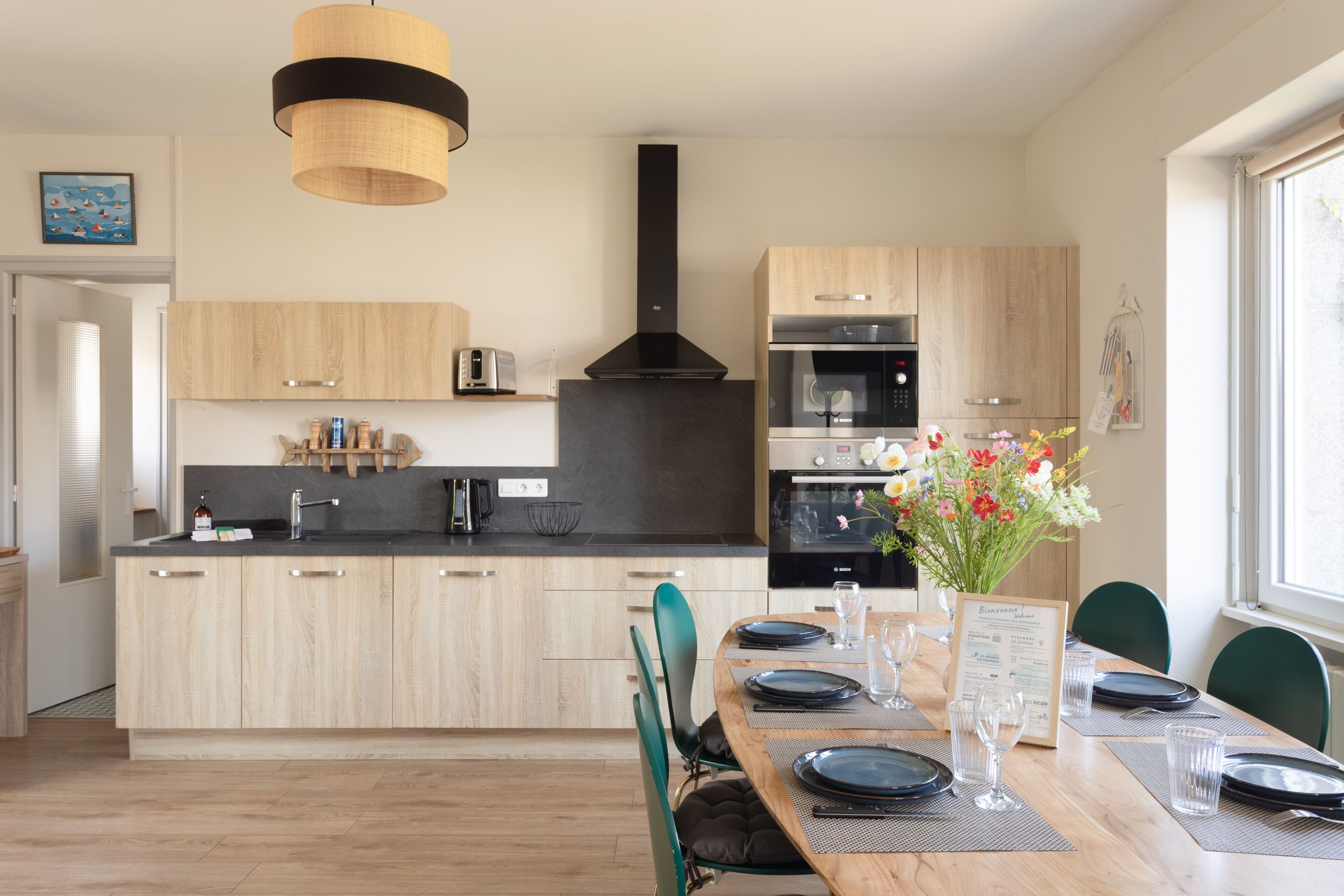 Una cocina moderna con armarios de madera, una campana extractora negra y un comedor con mesa de madera dispuesta para dos.