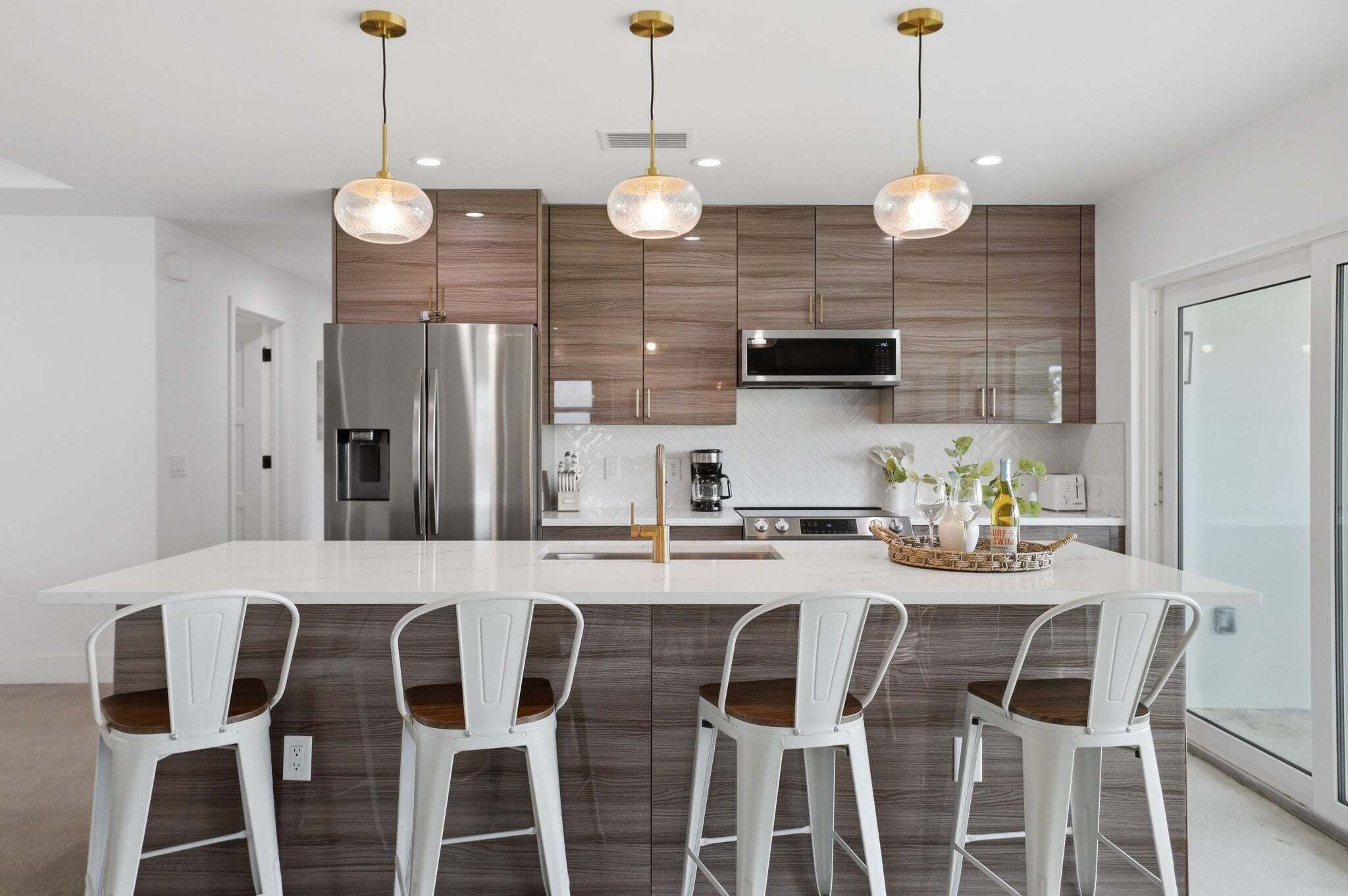 Une cuisine moderne dotée d’un îlot central, d’appareils électroménagers en acier inoxydable et de luminaires suspendus.
