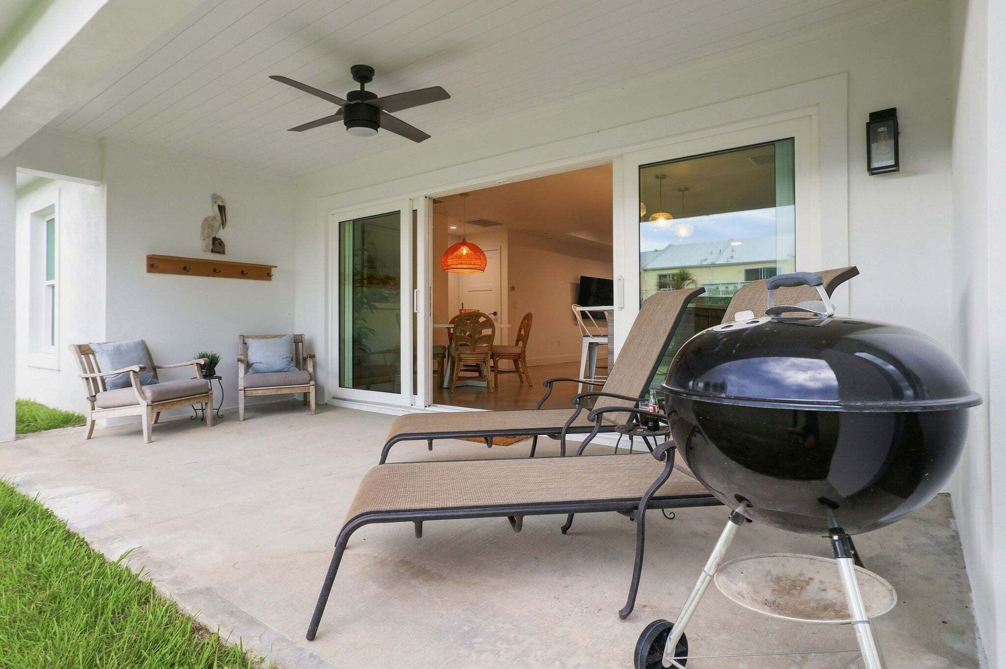 A covered outdoor seating area with a grill, chairs, and a ceiling fan.