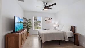 A bedroom with a bed, a television, a ceiling fan, a window with a view, and a potted plant. - 🌴 Spacious Coastal Retreat | Large Backyard, BBQ Grill & Outdoor Private Patio! (Fort Pierce)