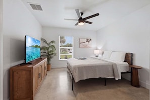 Ein Schlafzimmer mit einem Bett, einem Fernseher, einem Deckenventilator, einem Fenster mit Ausblick und einer Topfpflanze.