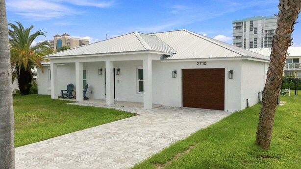 A single-story building with a flat roof, a covered porch, and a garage door. - 🌴 Spacious Coastal Retreat | Large Backyard, BBQ Grill & Outdoor Private Patio! (Fort Pierce)
