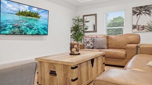 A living room with a television, a wooden coffee table, a sofa, and a plant. - 🌴 Spacious Coastal Retreat | Large Backyard, BBQ Grill & Outdoor Private Patio! (Fort Pierce)