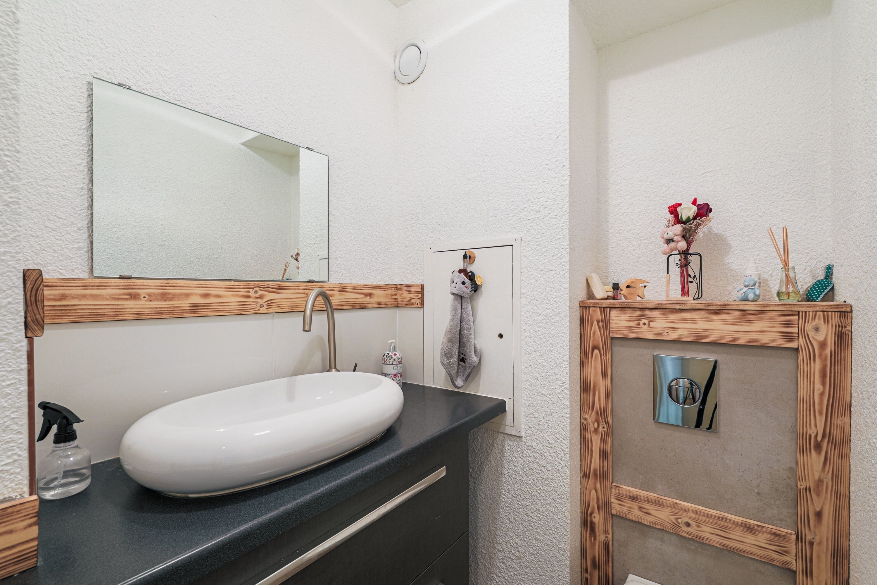 Un baño con un lavamanos blanco, un espejo y un mueble de tocador de madera.