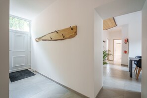 A hallway with a wooden wall art piece, a white door, and a glimpse of a dining area with a table and chairs. - Gîte La Petite Récré - Au pied des Hautes Vosges (Plainfaing)