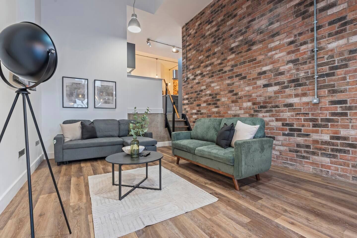 A modern living room with a brick wall, a grey sofa, a green sofa, a round coffee table, and a floor lamp.