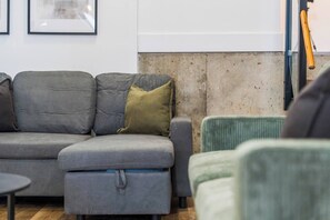 Ein graues Sofa mit einem grünen Kissen, ein kleiner Hocker und ein gerahmtes Bild an der Wand.