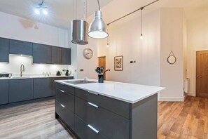 Een moderne keuken met een centraal eiland, donkere kastjes en hangende verlichting.