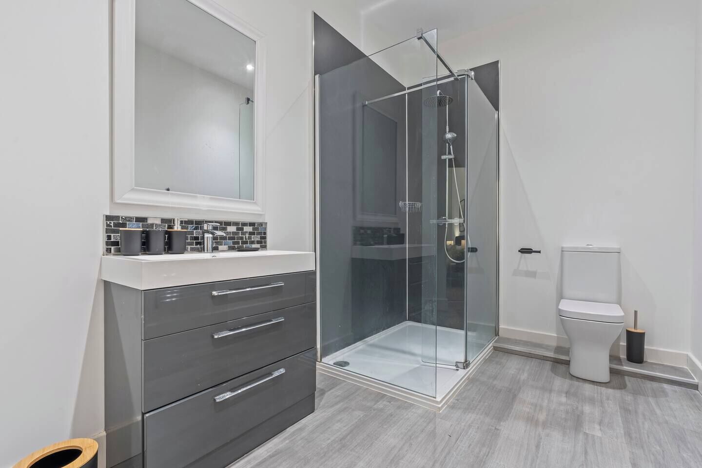 A modern bathroom with a glass-enclosed shower, a white toilet, and a dark-colored vanity with drawers.