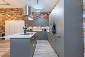 Eine moderne Küche mit einer zentralen Kochinsel, grauen Schränken, einer Wand in Backsteinoptik und Pendelleuchten.