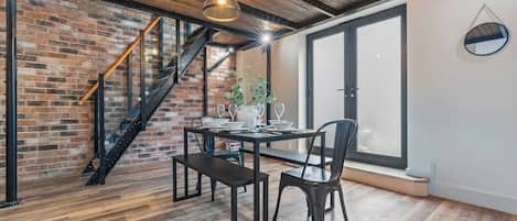 A dining area with a brick wall, wooden floor, a staircase, and pendant lighting.