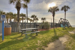 A beach access sign, a picnic table, a swing set, and a fenced area with palm trees. - Myrtle Beach Resort 147A (Myrtle Beach)