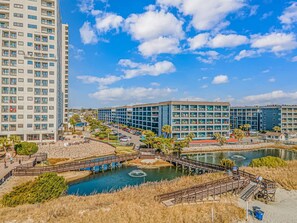A modern building complex with multiple floors, a parking area, and a water feature with a bridge. - Myrtle Beach Resort 147A (Myrtle Beach)
