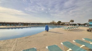 Una piscina con sillones de descanso y un área techada, rodeada por una cerca y palmeras.