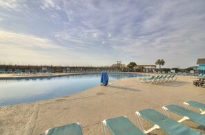 Ein Swimmingpool mit Liegestühlen und einem überdachten Bereich, umgeben von einem Zaun und Palmen.