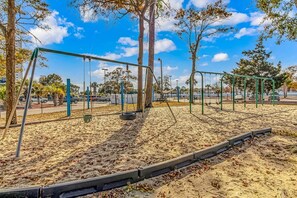 A playground with swings and tire swings on a sandy ground, surrounded by trees and a clear sky. - Myrtle Beach Resort 147A (Myrtle Beach)