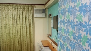 Ein Zimmer mit einem Bett, einem Schreibtisch, einem Stuhl, einer Klimaanlage und einem wandmontierten Fernseher.