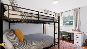 A bunk bed with striped bedding, a desk with a chair, a window with curtains, and a patterned rug.