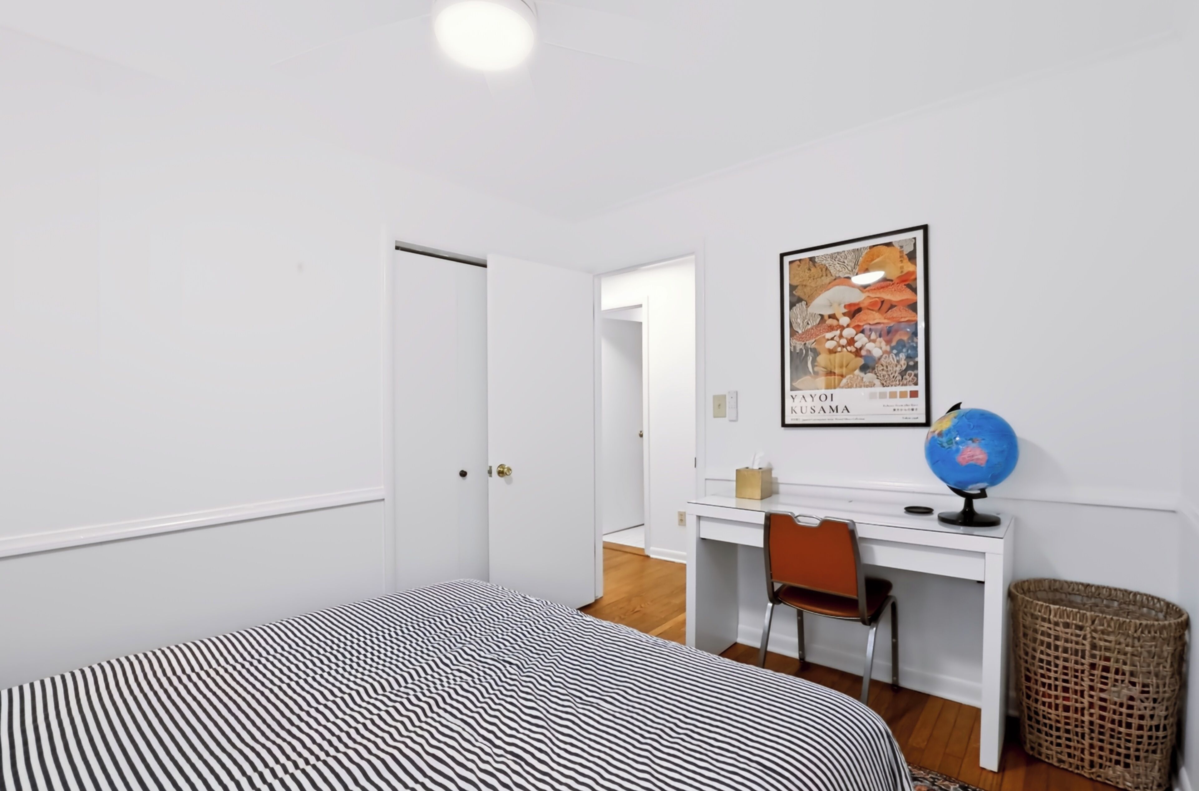 Une pièce comprenant un lit, un bureau, une chaise, un globe terrestre et un tableau encadré accroché au mur.