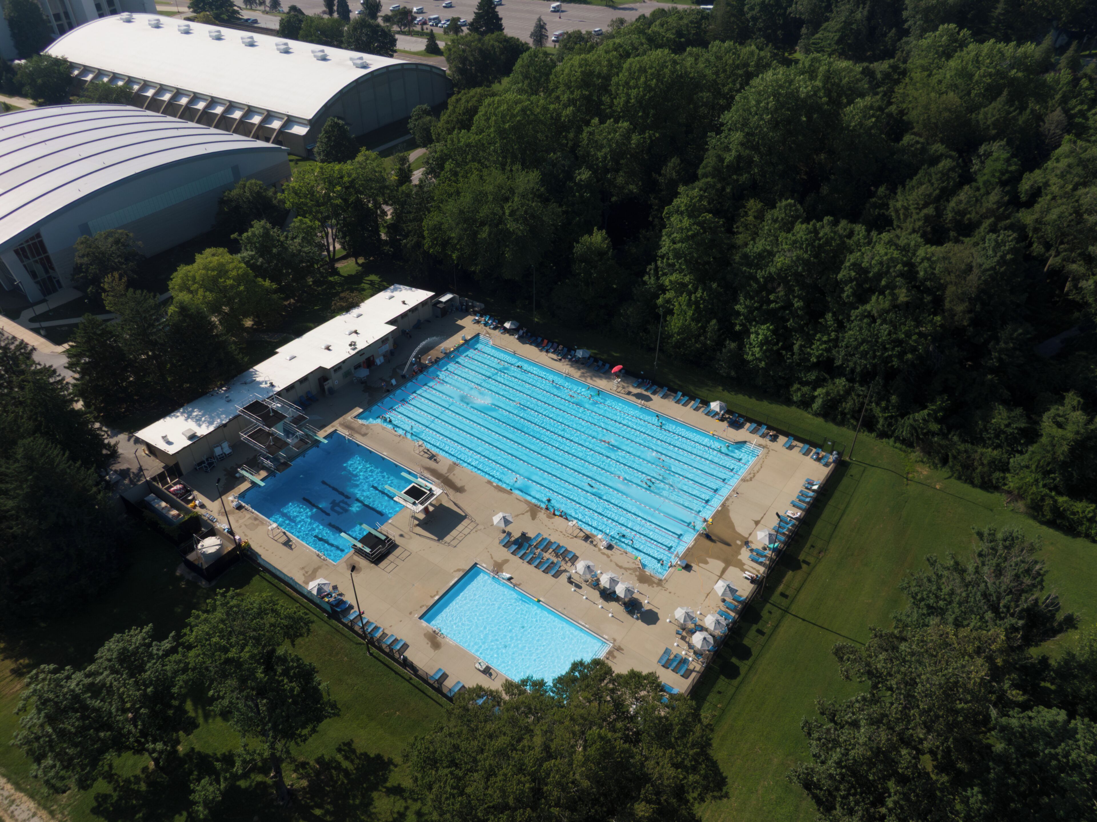 An aerial view of a swimming pool complex with multiple pools and lounge areas, surrounded by trees.