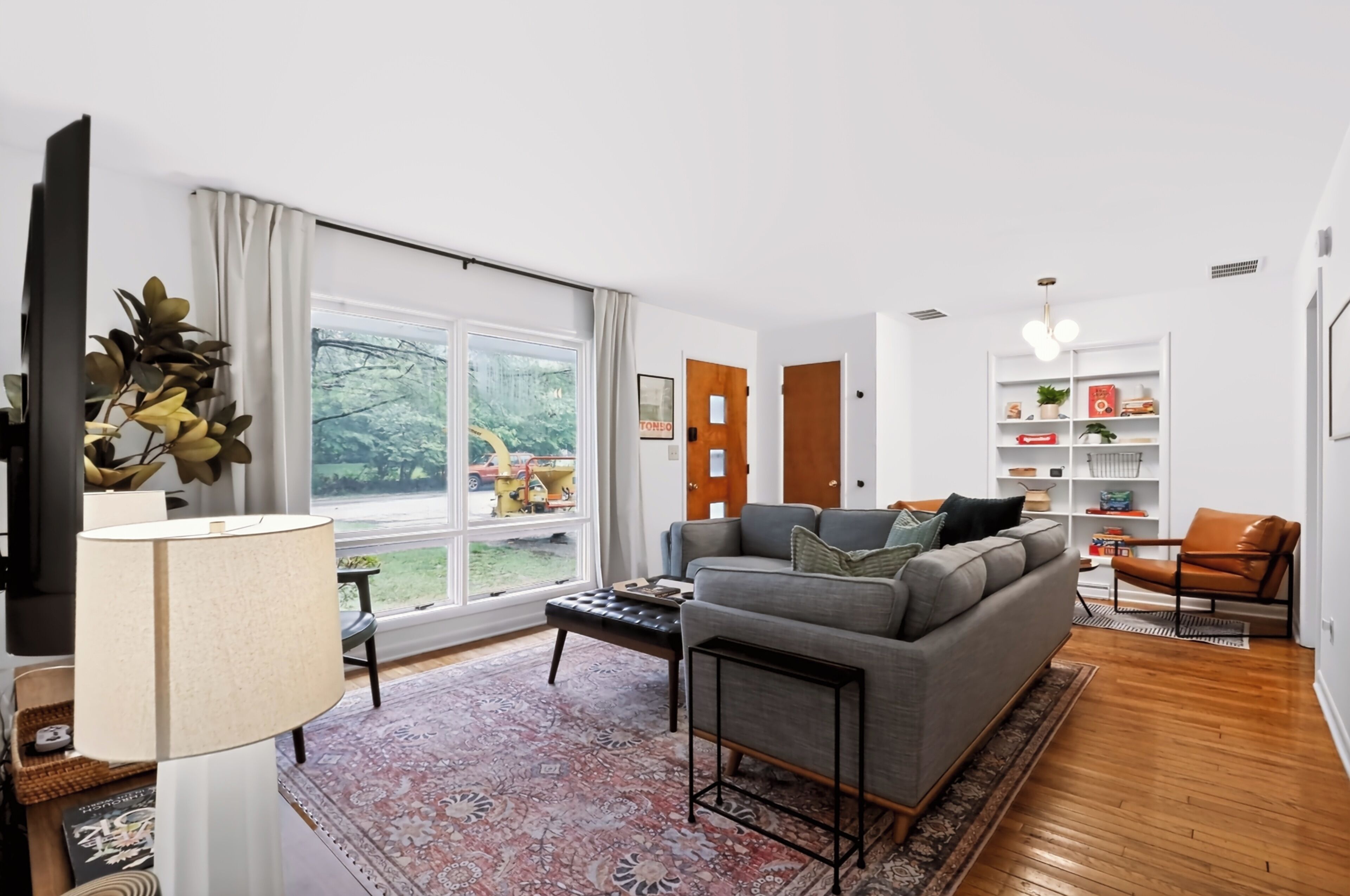 Een moderne woonkamer met een groot raam, een grijze bank, een salontafel en een boekenkast.
