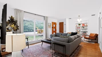 Een moderne woonkamer met een groot raam, een grijze bank, een salontafel en een boekenkast.