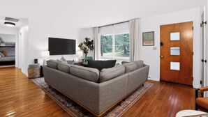 A modern living room with a grey sofa, a flat-screen TV, and a wooden door. - Close to campus. Awesome hangout home! (Bloomington)