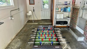 A room with a foosball table, a white chair, a shelf with cleaning supplies, and a door with a window. - Close to campus. Awesome hangout home! (Bloomington)