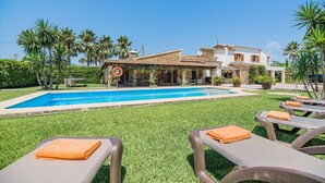 A pool area with lounge chairs and a building with a tiled roof. - Elegant Pool Villa in Alcudia (Alcúdia)