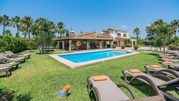 A pool area with lounge chairs and a building with a tiled roof. - Elegant Pool Villa in Alcudia (Alcúdia)