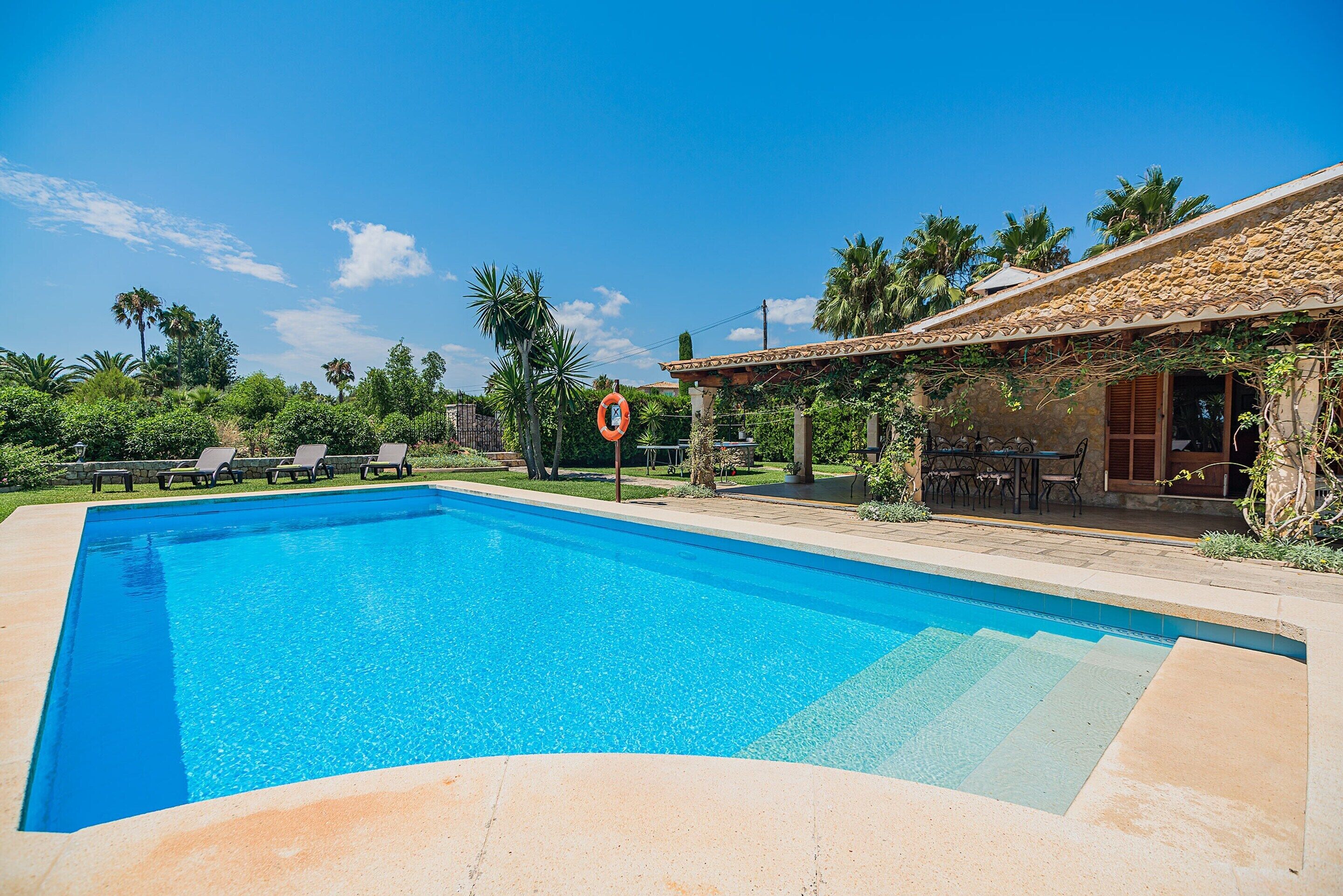 Una piscina blava i cristal·lina amb gandules i un senyal de vida, envoltada de vegetació i un edifici de pedra.