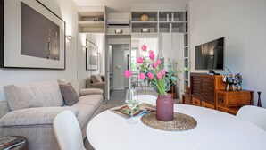 Una sala de estar moderna con un sofá blanco, una mesa de comedor con un jarrón de flores y un televisor en la pared.