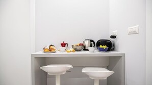 Una encimera de cocina con cafetera, hervidor y cuencos con fruta.