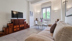 Una sala moderna con un televisor de pantalla plana, muebles de madera, una zona de comedor con una mesa y sillas, y un ventanal con vistas.