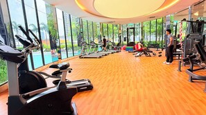 A gym with cardio machines, weightlifting equipment, and a large windowed wall providing a view of greenery. - Trion KL Residence Pearl Suites (Kuala Lumpur)