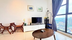 A modern living room with a flat-screen TV, wooden chairs, a small table, and a view of a cityscape through large windows. - Trion KL Residence Pearl Suites (Kuala Lumpur)