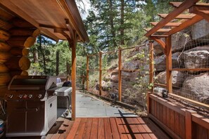 A wooden deck with a grill and a fenced area with rocks and trees.