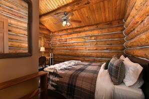 A log cabin bedroom with a bed, a desk, and a ceiling fan.