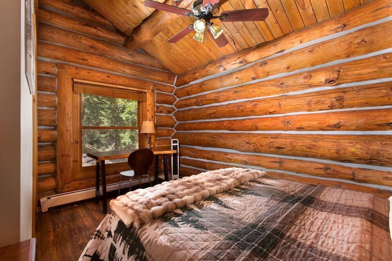 Ein Zimmer in einer Blockhütte mit einem Bett, einem Schreibtisch und einem Stuhl.