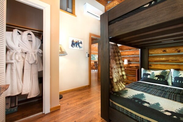 A bedroom with a bed, a wooden headboard, a closet with a robe, and a painting on the wall.