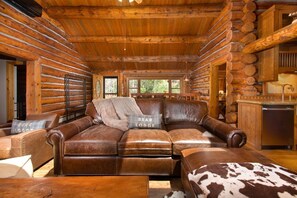 A log cabin interior with a leather sofa, a cowhide rug, and a kitchen area.