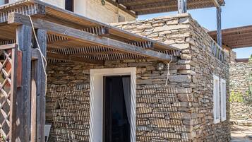 Ein Steinhaus mit einem hölzernen Pergola-Eingang und einem kleinen Garten mit rosa Blumen.