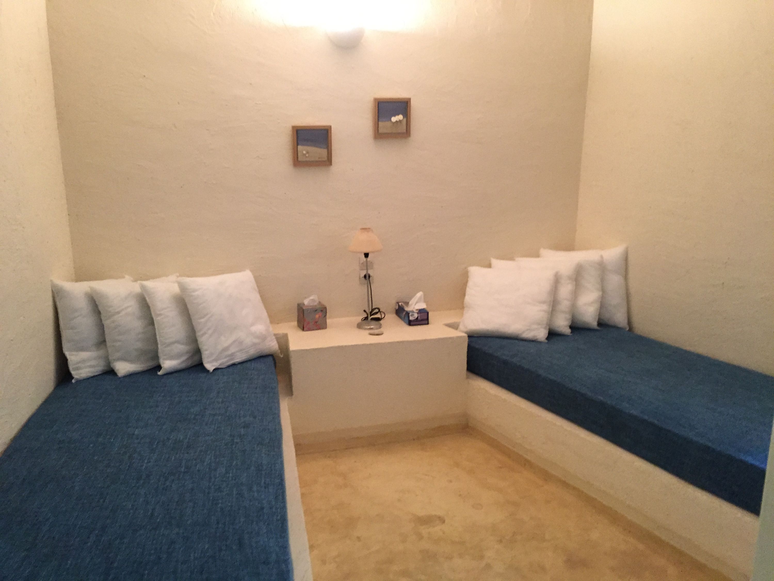 Ein kleines Zimmer mit zwei Einzelbetten, einem Nachttisch mit Lampe und zwei gerahmten Bildern an der Wand.